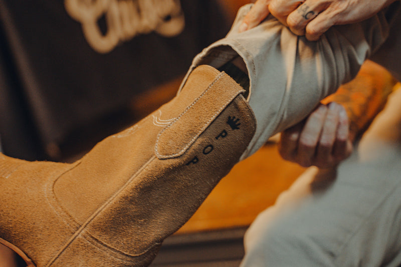 Close-up of hands on a tan cowboy boot at Chisos HQ